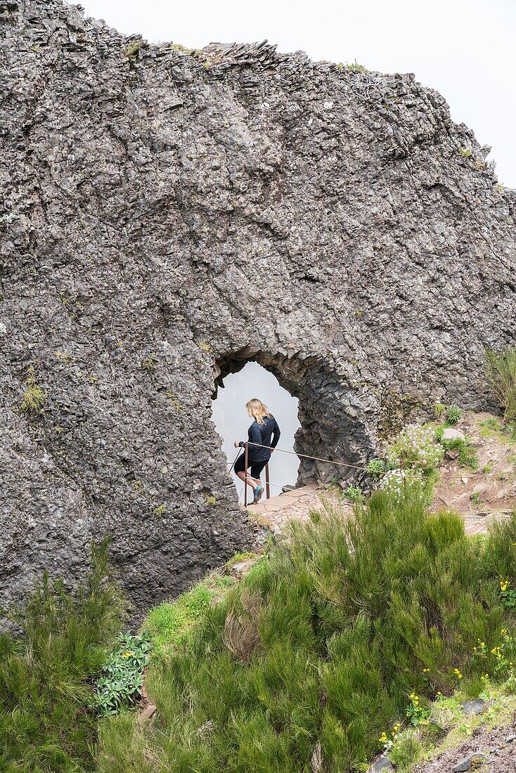 Woman passing through a rock tunnel on the trail at Pico do Areeiro. Funchal, Madeira region, Portugal.