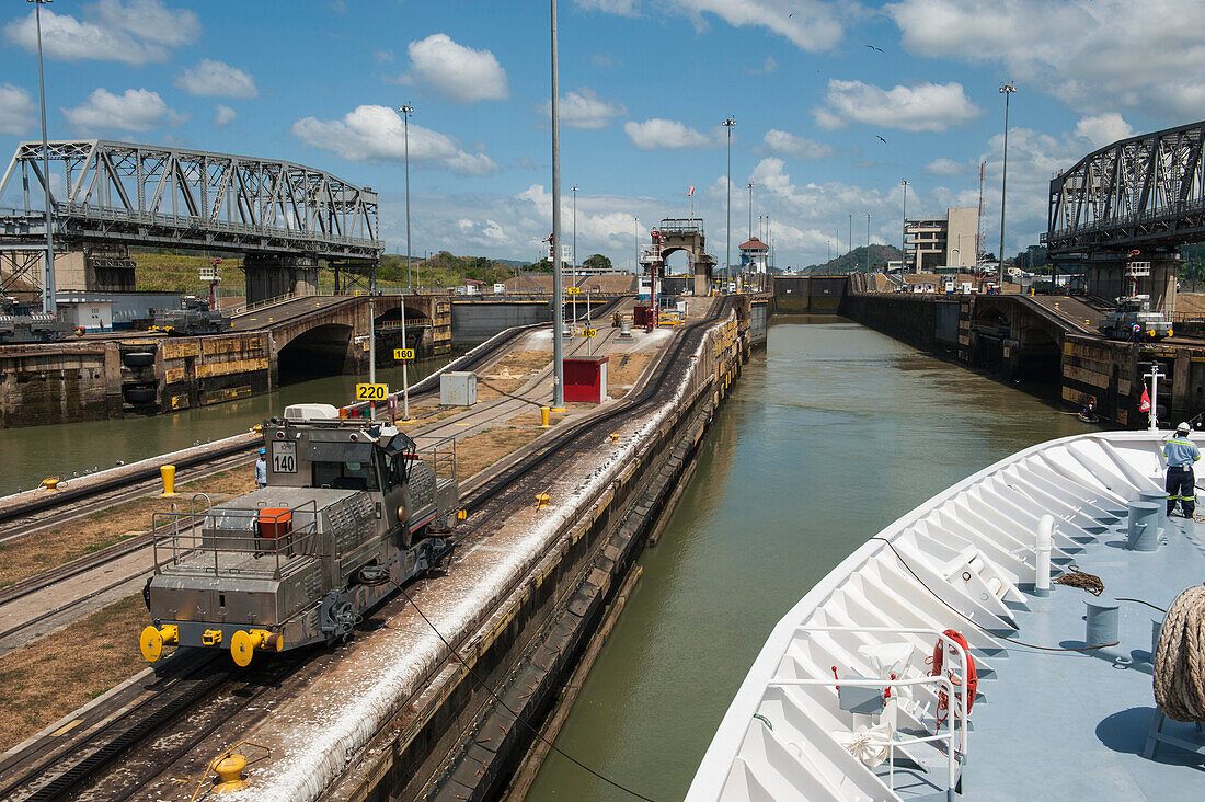 Das Expeditions-Kreuzfahrtschiff MS Hanseatic (Hapag-Lloyd Cruises), verbunden mit elektrischen Lokomotiven (sogenannte Maultiere), bei der Einfahrt in die Schleuse Miraflores Locks auf der Westseite des Panamakanals, Panama City, Panama, Mittelamerica