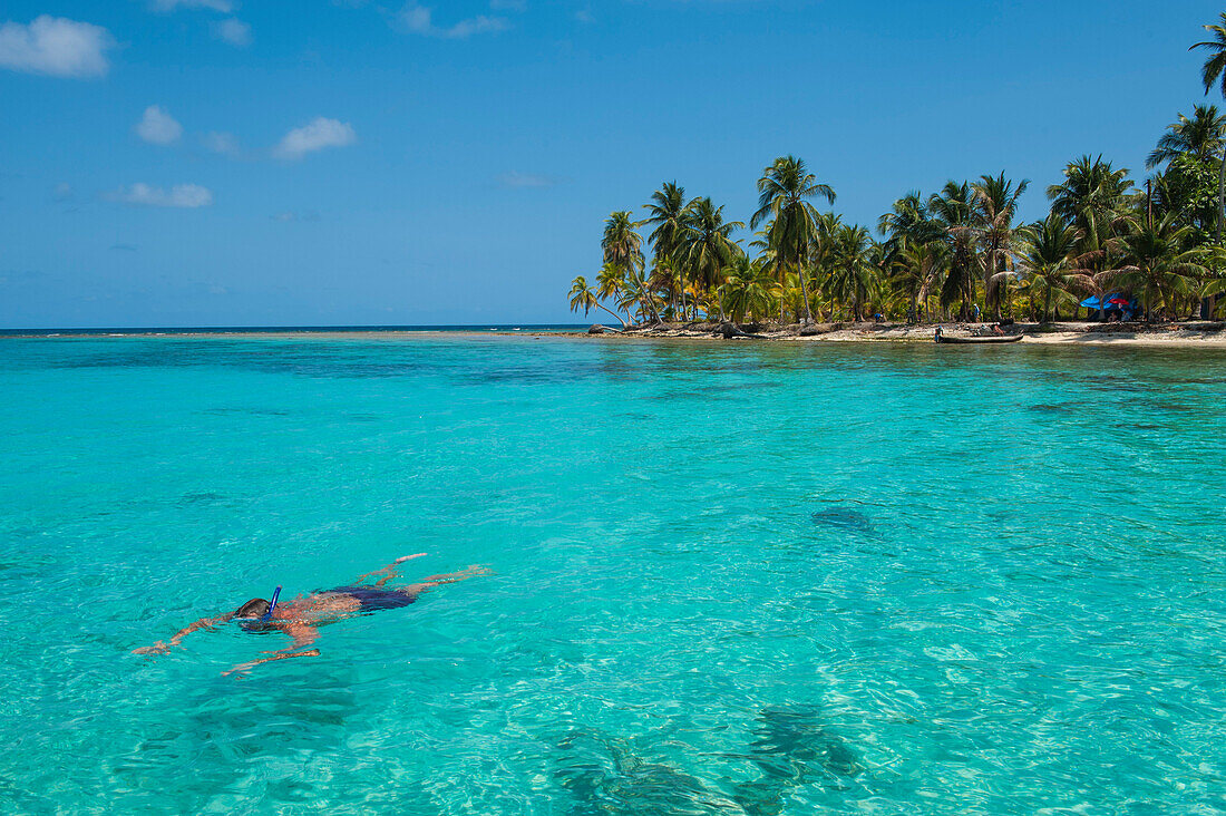 Ein Schnorchler schwimmt im türkisfarbenen Wasser vor der Küste einer kleinen von Palmen übersäten Insel, San Blas-Inseln, Panama, Mittelamerika