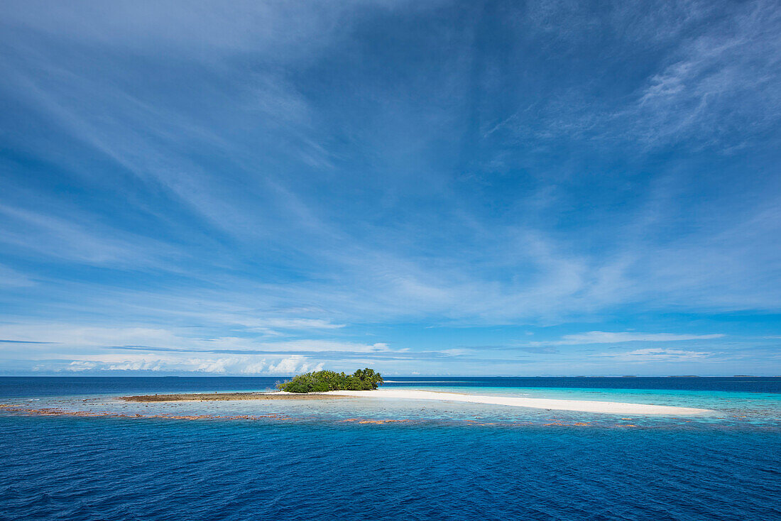 Blick auf eine winzige mit Bäumen bestückter Insel, umgeben von Korallenriffen und einem langen weißen Sandstrand, der von einem blauen Himmel mit luftigen dünnen Wolken dominiert wird, Likiep Atoll, Ratak-Kette, Marshallinseln, Südpazifik