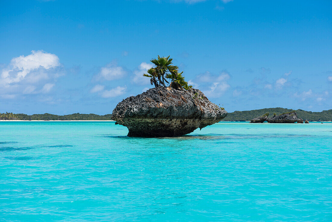 Eine winzige pilzförmige Insel, die von mehreren Palmen gekrönt wird, befindet sich zwischen türkisfarbenem Wasser mit großer Insel im Hintergrund, Fulaga Island, Lau Group, Fidschi, Südpazifik
