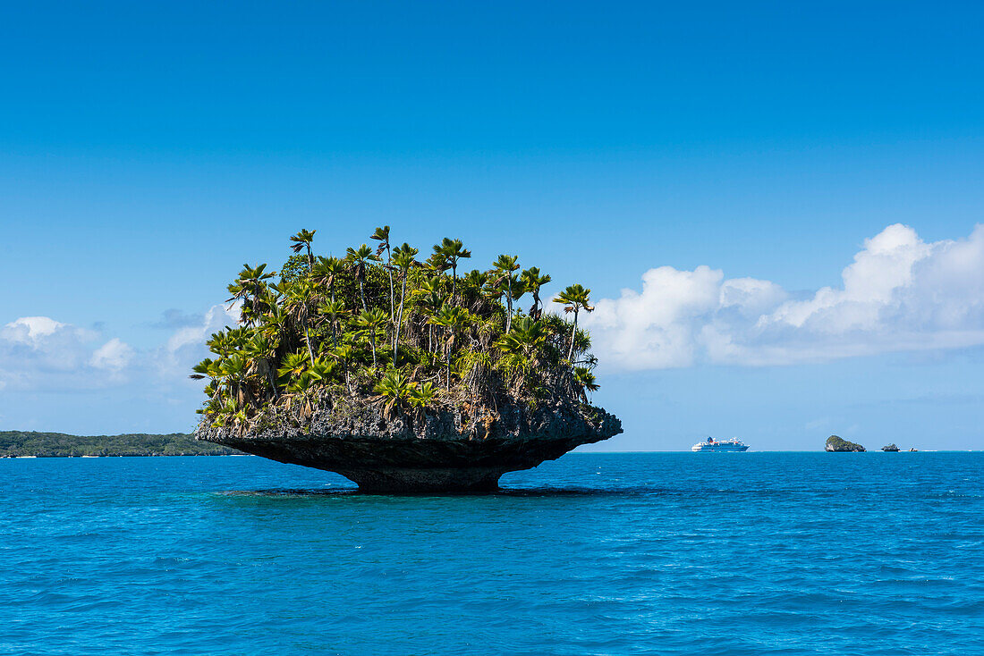 Eine kleine pilzförmige Insel mit Palmen und Büschen liegt im türkisfarbenen Wasser, im Hintergrund das Expeditions-Kreuzfahrtschiff MS Bremen (Hapag-Lloyd Kreuzfahrten), Fulaga Island, Lau Group, Fidschi, Südpazifik