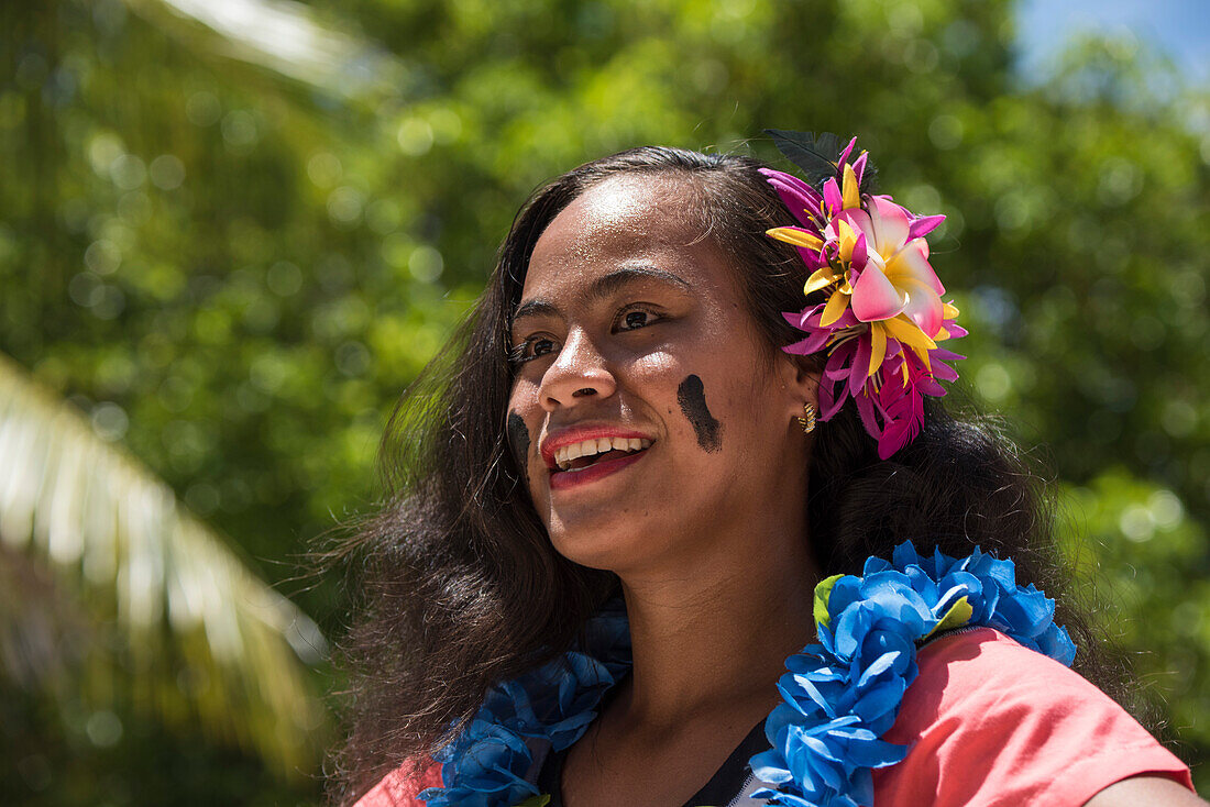 A beautiful smiling woman with black streaks on her cheeks, a colorful flower in her hair, and a blue lei around her neck, prepares to greet visitors from an expedition cruise ship, Fagamalo, Savai'i, Samoa, South Pacific