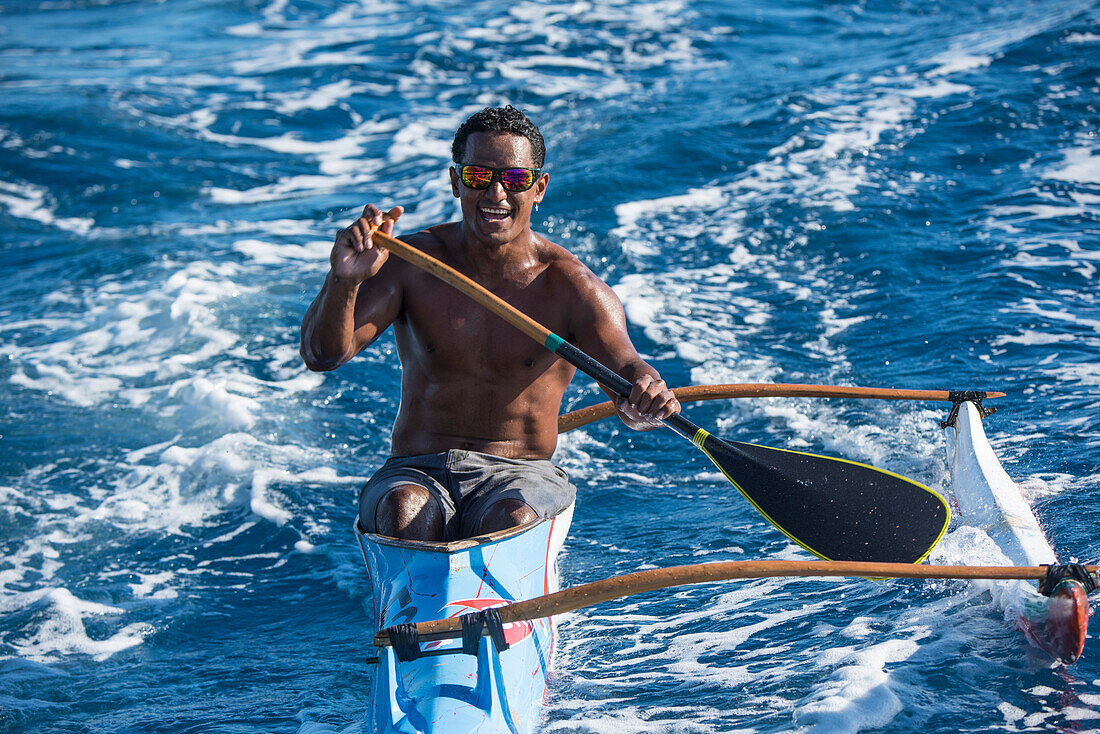 A young man wearing reflector sunglasses and paddling a single-rigger kayak smiles at the camera, Bora Bora, Society Islands, French Polynesia, South Pacific