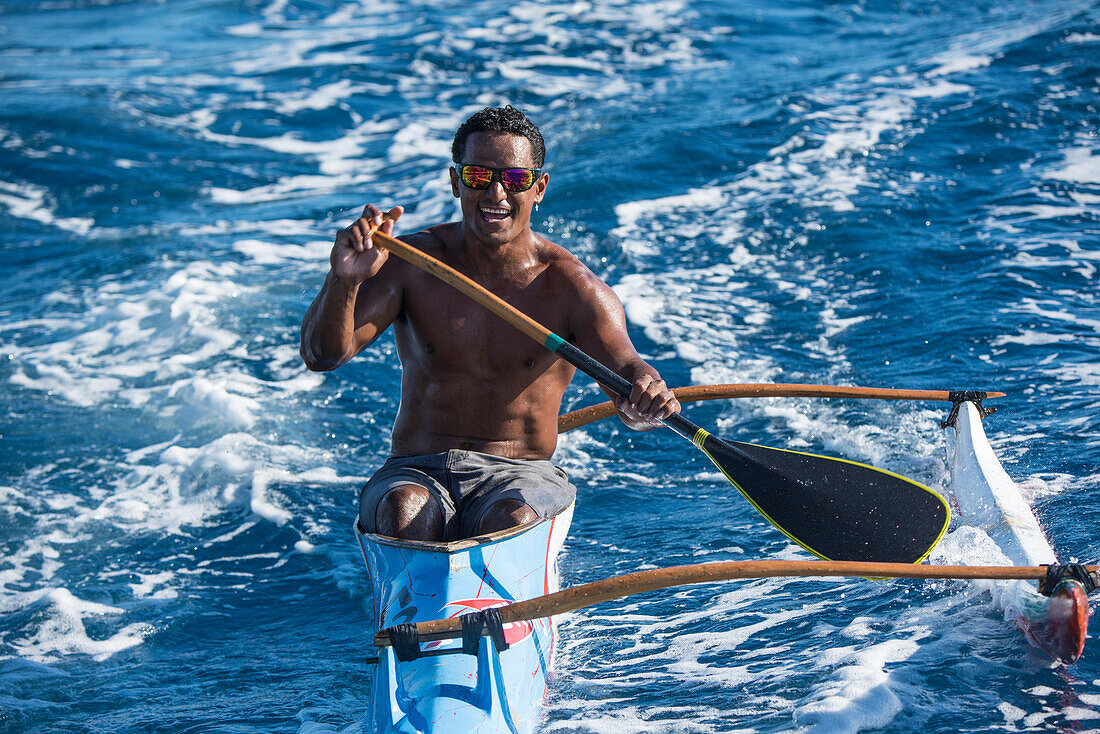 Ein junger Mann der eine Reflektor-Sonnenbrille trägt und mit einem Single-Rigger-Kajak paddelt, lächelt in die Kamera, Bora Bora, Gesellschaftsinseln, Französisch-Polynesien, Südpazifik