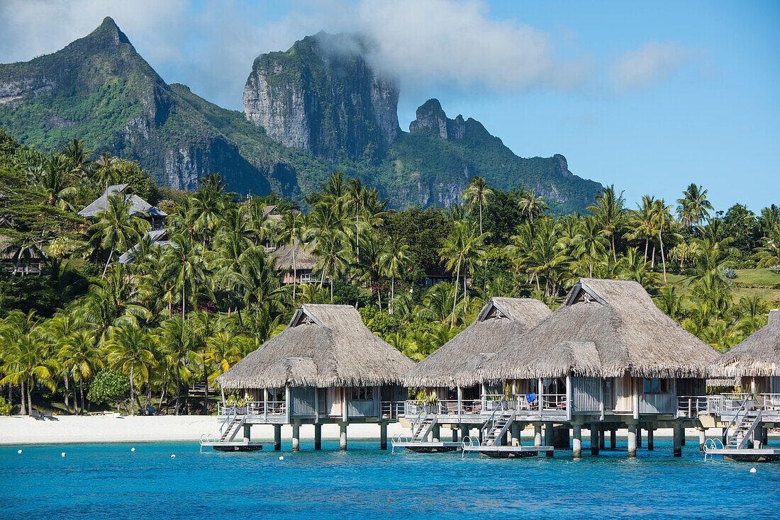 Überwasser Bungalows eines Luxusresorts auf Stelzen werden von den hohen Bergen im Hintergrund in den Schatten gestellt, Bora Bora, Gesellschaftsinseln, Französisch-Polynesien, Südpazifik