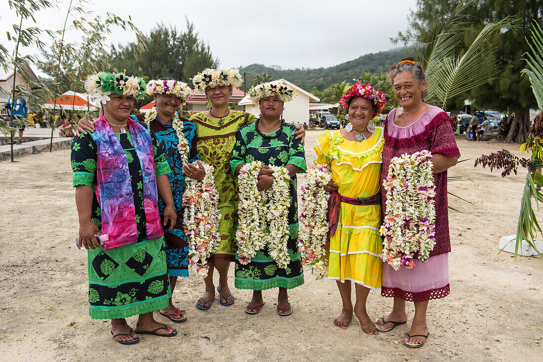 Eine Gruppe hell gekleideter Frauen, von denen die meisten lächeln, Kopfschmuck tragen und Leis halten, stehen dem Betrachter gegenüber, Rurutu, Austral-Inseln, Französisch-Polynesien, Südpazifik