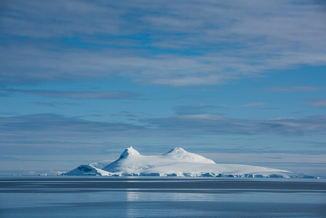 Blick auf eine Insel mit zwei Bergspitzen unter blauem Himmel mit dünnen Wolken, Wilhelmina Bay, Antarktische Halbinsel, Antarktis