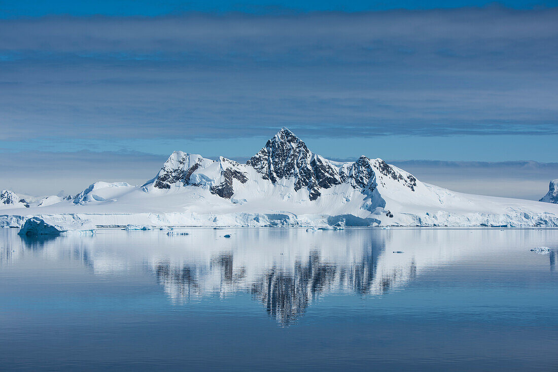 In einem seltenen, nahezu windstillen Moment verzaubert ein Spiegelbild schneebedeckter Berge mit einem zentralen, hohen Gipfel das Auge, Wilhelmina Bay, Antarktische Halbinsel, Antarktis