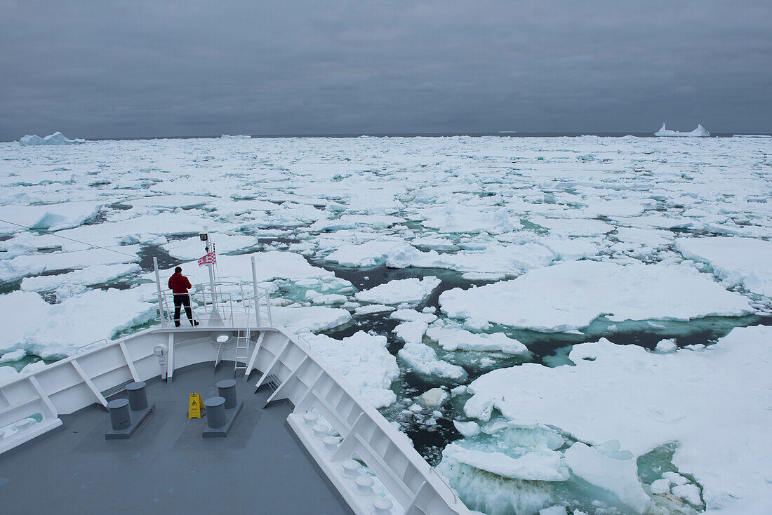 Ein einsamer Mensch steht auf der sogenannten 'Affenbrücke' des Expeditions-Kreuzfahrtschiffes MS Bremen (Hapag-Lloyd Kreuzfahrten) in einer Masse an Meereis, nahe Laurie Island, Südlich Orkney-Inseln, Antarktis