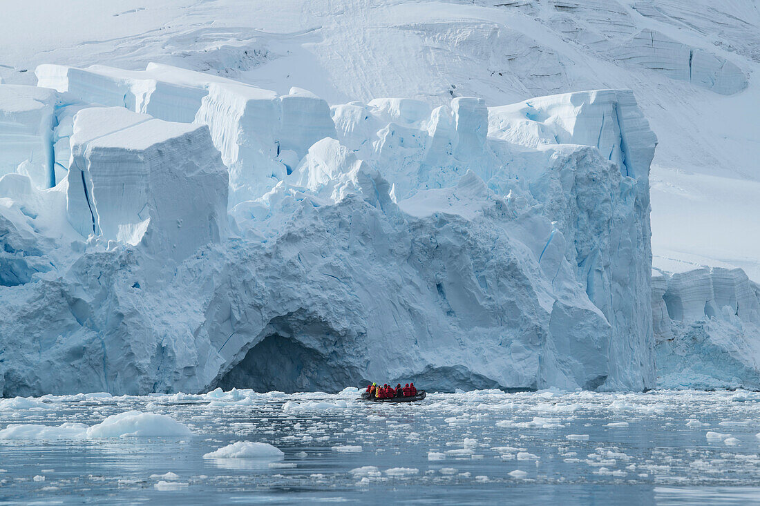 A Zodiac dinghy raft with passengers cruises through floating ice in front of a massive glacier front, Paradise Bay (Paradise Harbor), Danco Coast, Graham Land, Antarctica