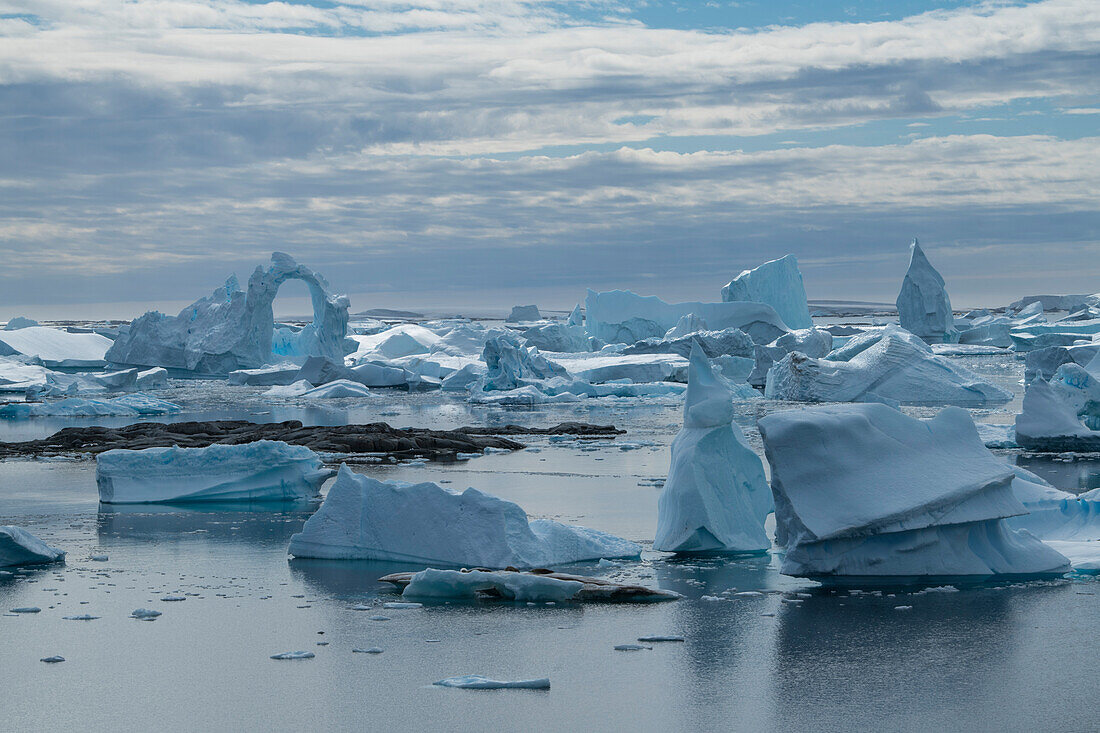 In a scene of oddly formed icebergs, one features a delicate looking archway at least 20 meters high, Pleneau Island, Wilhelm Archipelago, Antarctica