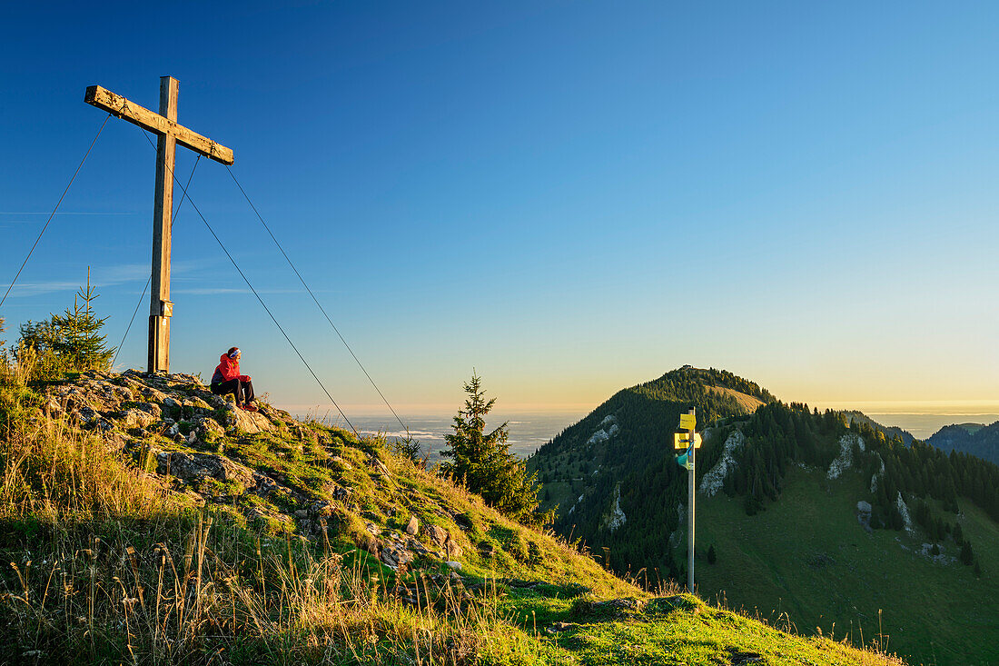 Frau beim Wandern sitzt am Gipfel des Feichteck, Hochries im Hintergrund, Feichteck, Chiemgauer Alpen, Oberbayern, Bayern, Deutschland