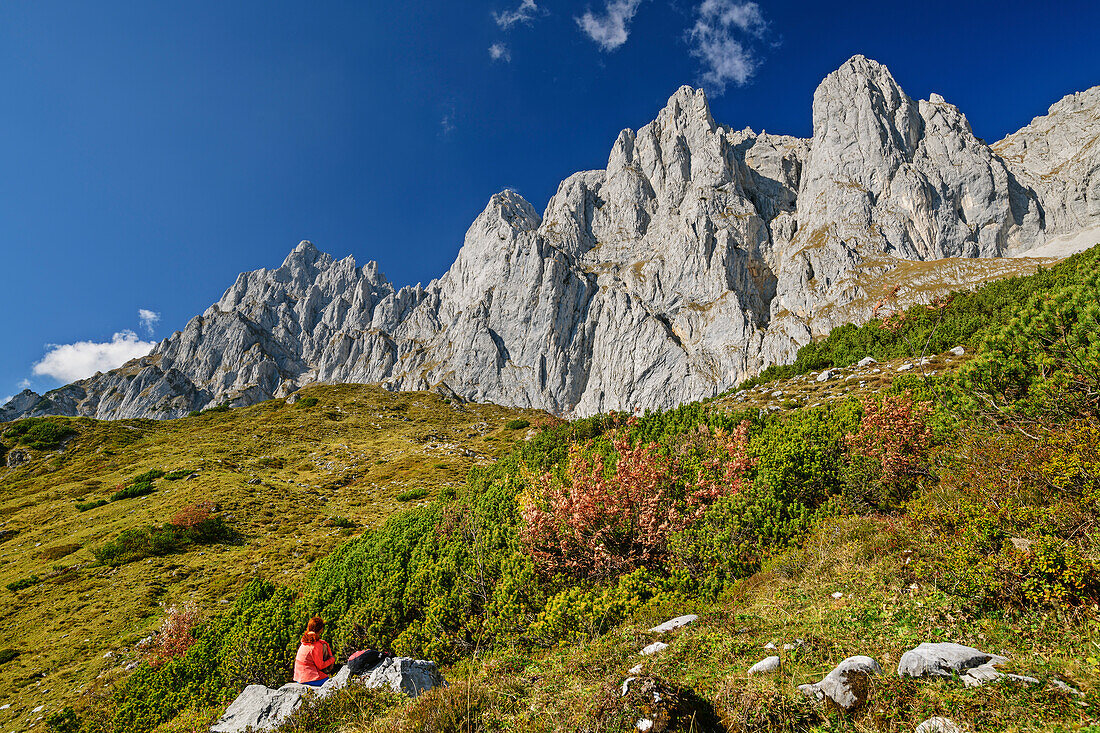 Woman hiking sitting on rock and looking towards rock walls of Kaiser, Wilder Kaiser, Kaiser range, Tyrol, Austria