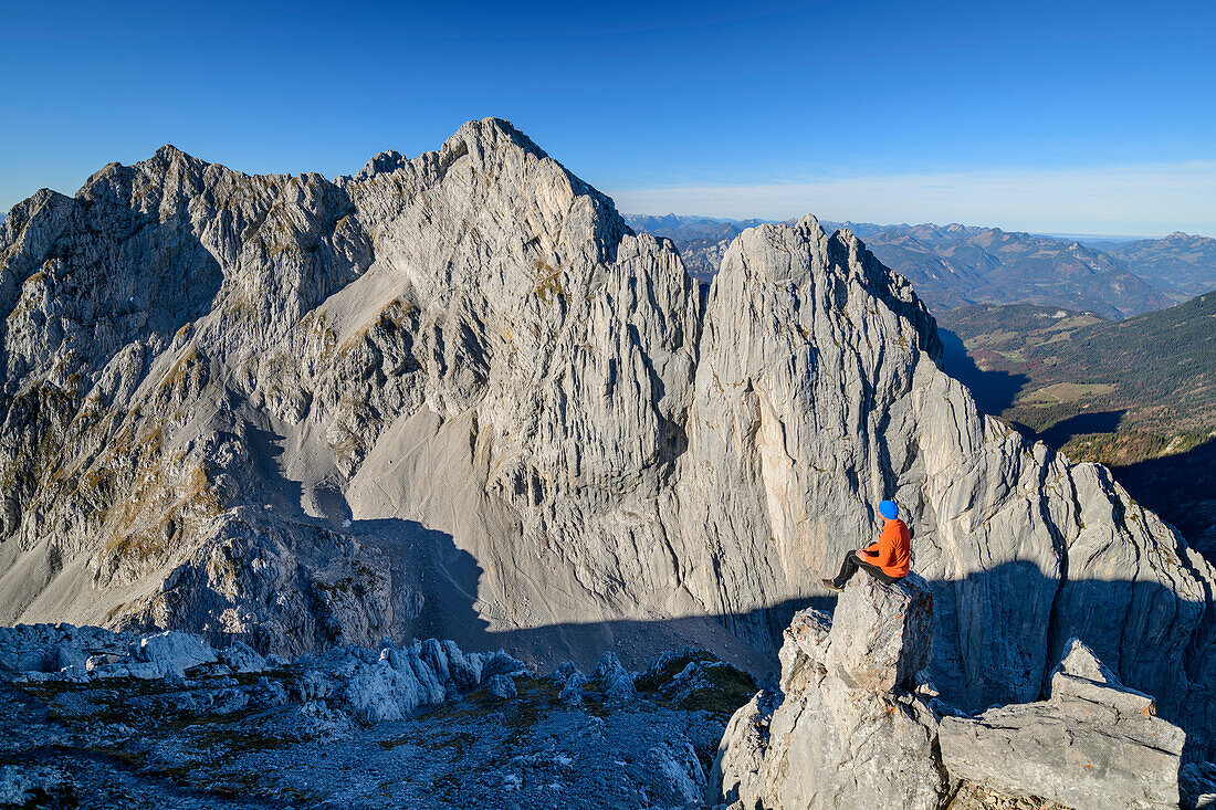 Man sitting on rock spire and looking towards rock walls of Vordere and Hintere Karlspitze, from Hintere Goinger Halt, Wilder Kaiser, Kaiser range, Tyrol, Austria