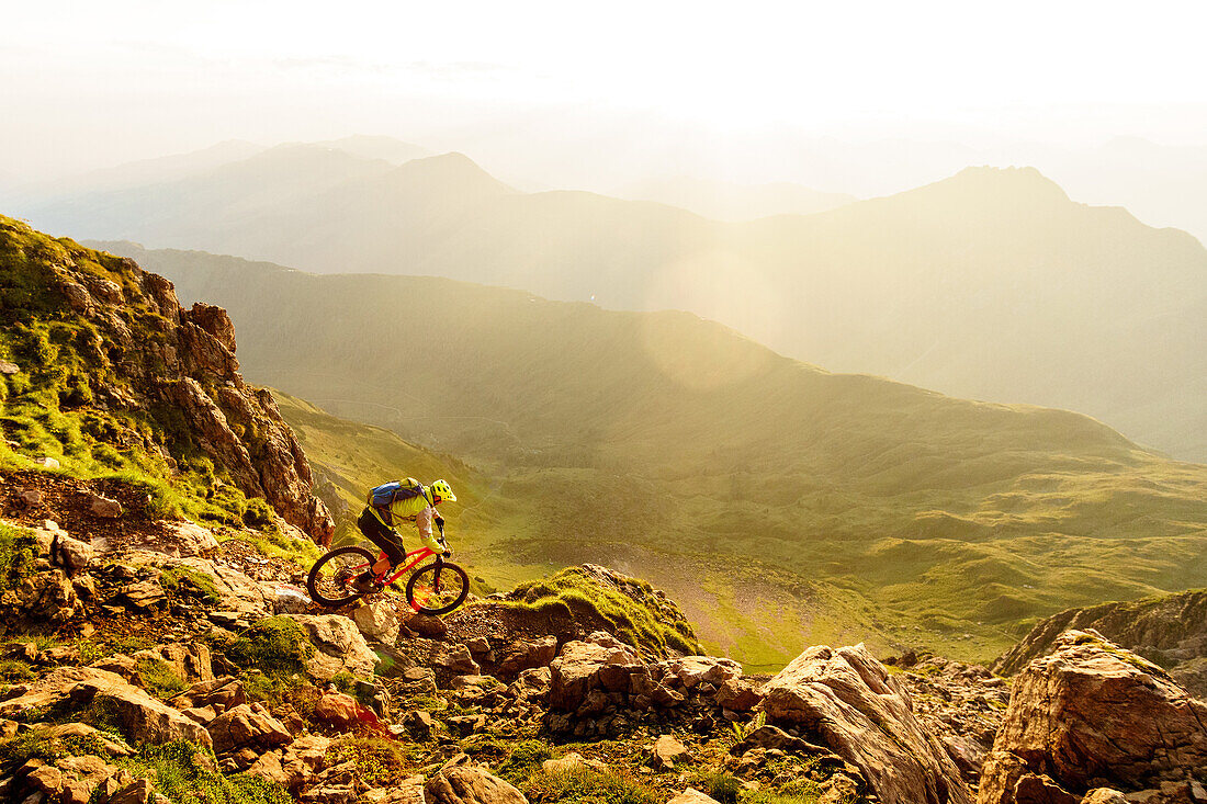 Mann mittleren Alters fährt einen anspruchsvollen Bergpfad mit dem Rad herunter, warmes Morgenlicht, Kirchberg, Tirol, Österreich