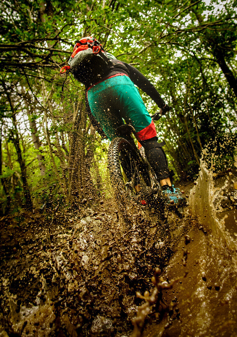 Mountainbiker paces through a deep mud hole, sprinkling mud, dirt and water, Finale Ligure, Italy