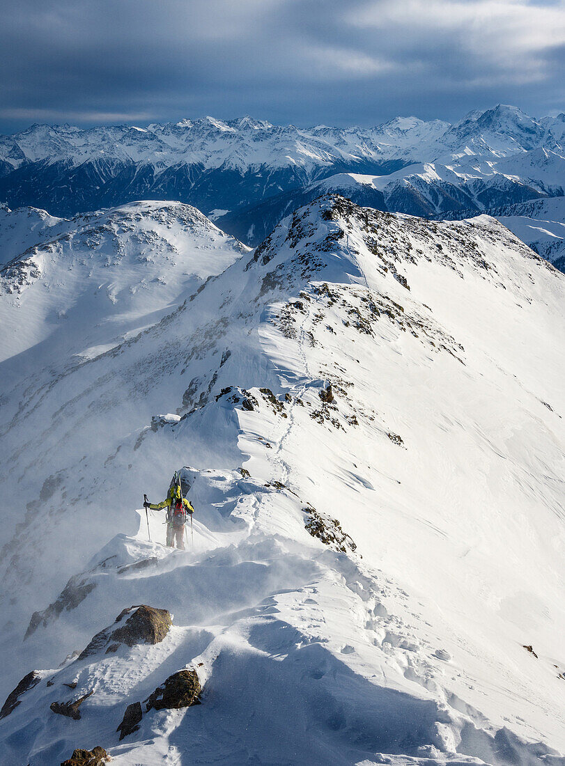 Junger Skibergsteiger auf einem Bergrücken mit auf den Rucksack geschnallten Ski bei stürmischen Witterungsverhältnissen, Sesvenna Gruppe, Vinschgau, Südtirol, Italien