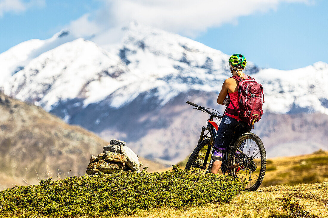 Young woman takes a break on her mountainbike and enjoys the view over the Ortler mountains, Bormio, Sondrino,Lombardia, South Tyrol, Italy