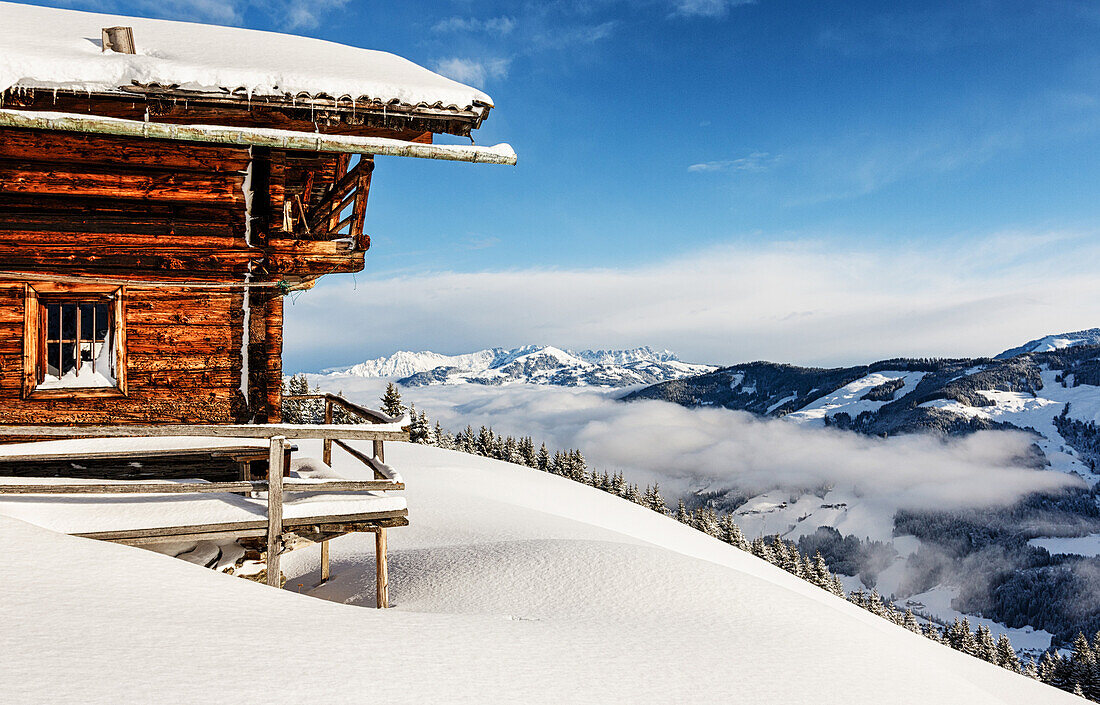 Eingeschneite Hütte über dem Tal mit Nebelschwaden im Langen Grund, Kelchsau, Kitzbühler Alpen, Tirol, Österreich