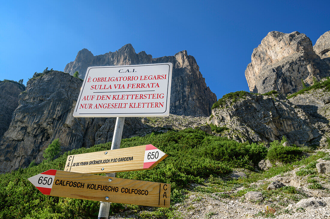 Wegweiser und Hinweistafel auf Klettersteig mit Felstürmen der Sella im Hintergrund, Pisciadu-Klettersteig, Sella, Dolomiten, UNESCO Welterbe Dolomiten, Südtirol, Italien