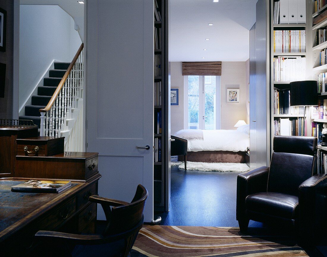 A desk and a leather armchair in front of open doors with a view into a bedroom and a stairwell