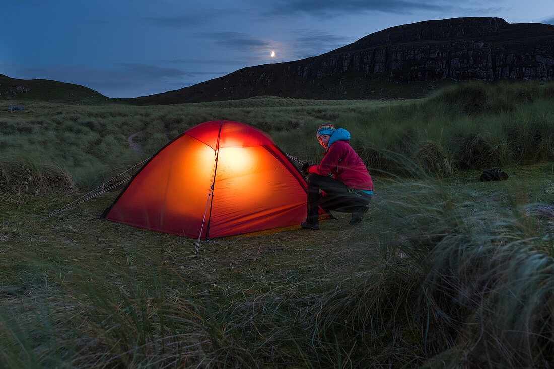 Eine Frau vor beleuchtetem Zelt, Sandwood Bay, Highlands, Schottland, Großbritannien