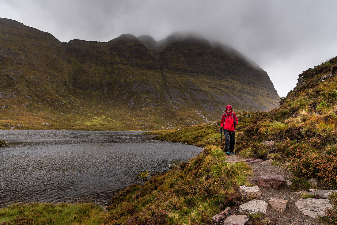 A female walker on the shore of a small lake below the Suilven, Inverpolly Nature Reserve, Highlands, Scotland, UK