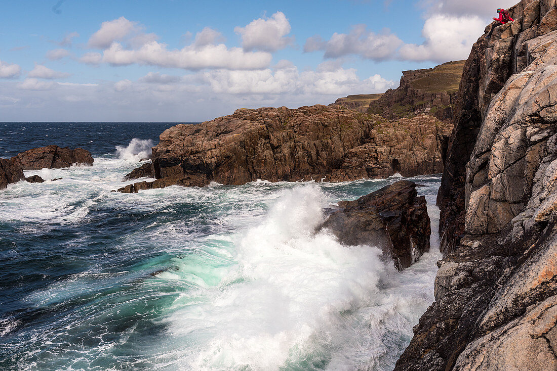 A woman looks from a rock on the surf breaking waves at Sheigra, Highlands, Scotland, UK