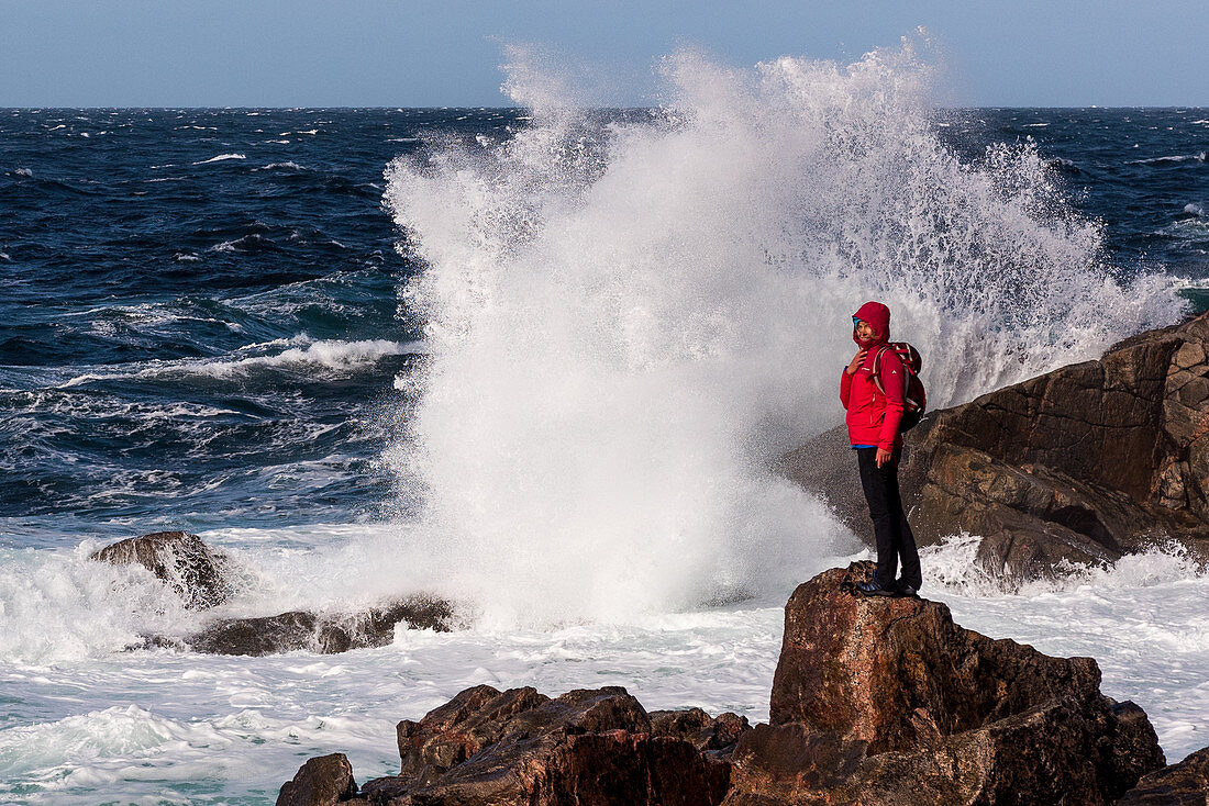 A woman is standing on a rock in front of the surf breaking waves at Sheigra, Highlands, Scotland, UK