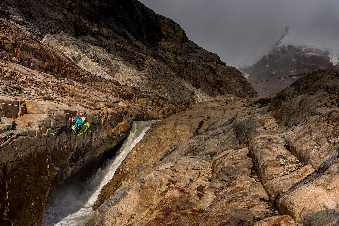 Eine Wanderin überquert den Rio Electrico an einer Seilrutsche (Tirolesa), Felsen im Vordergund, Nationalpark Los Glaciares, Patagonien, Argentinien