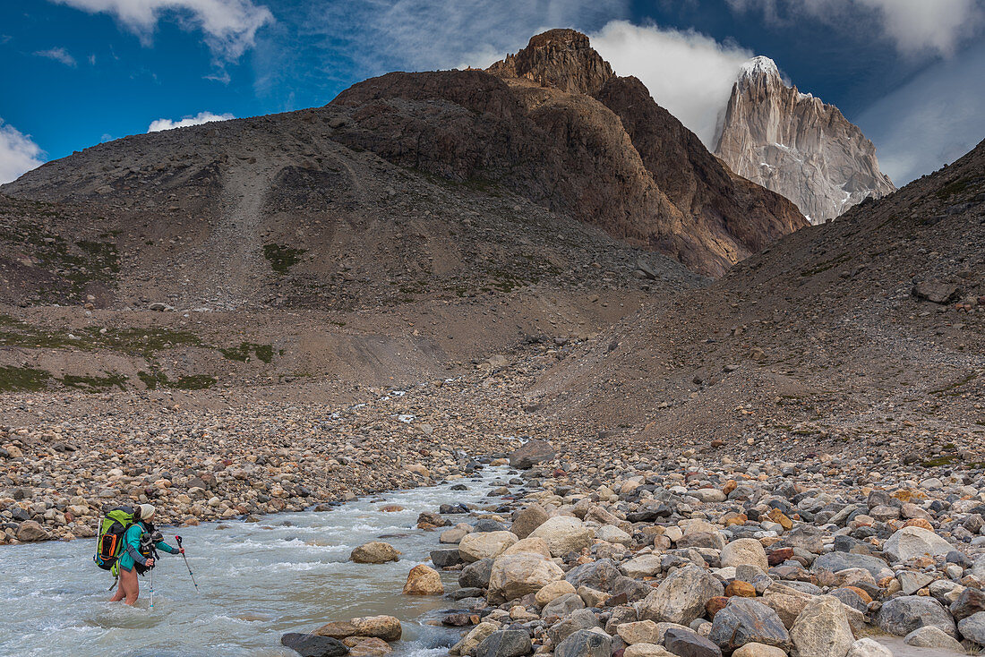 A female hiker crosses the Pollone River, overlooking Fitz Roy, Los Glaciares National Park, Patagonia, Argentina