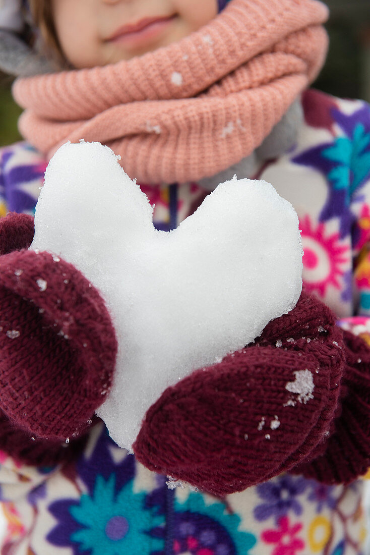 Hände eines Mädchens halten ein Herz aus Schnee