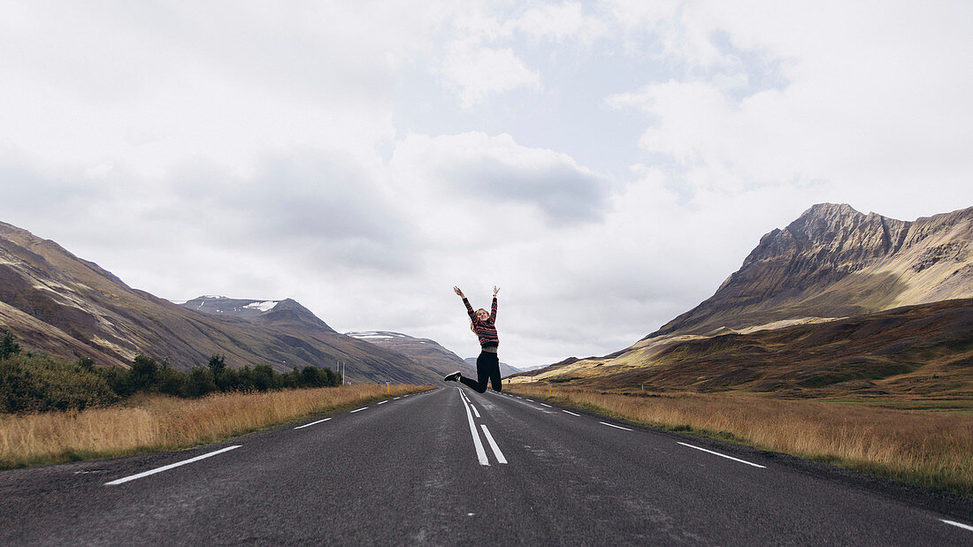 Eine Frau springend auf einer Landstraße in Island