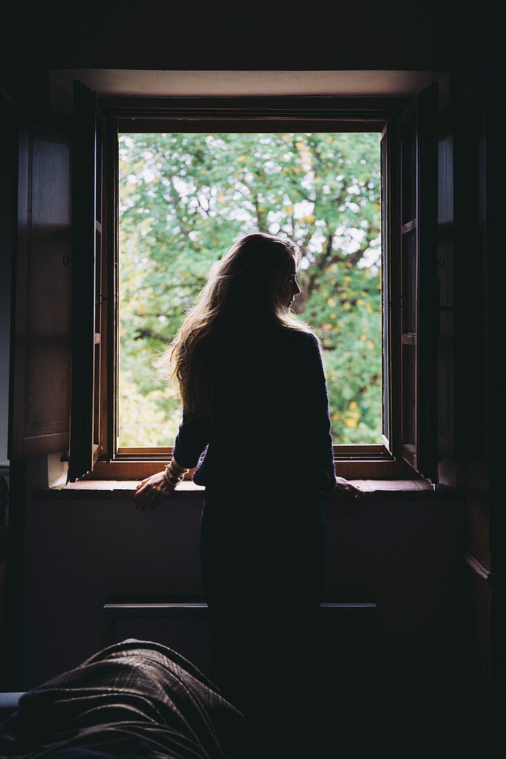 Junge Frau schaut aus einem Fenster eines Bauernhauses nahe Montefollonico, Provinz Siena, Toskana