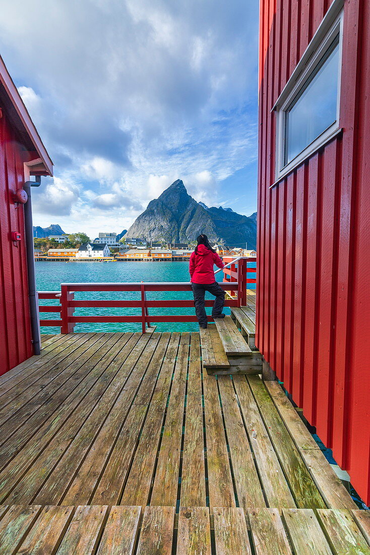 Woman on wooden deck look towards Sakrisoy and Olstinden mountain, Reine, Nordland, Lofoten Islands, Norway