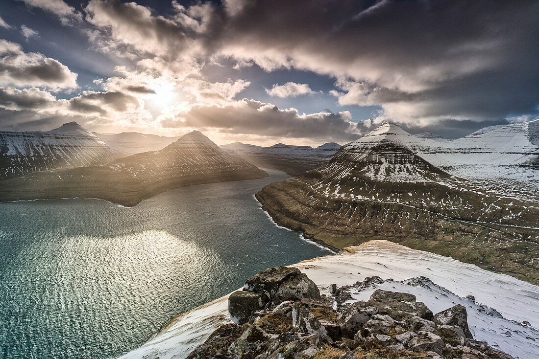 Sonnenstrahlen über den schneebedeckten Gipfeln entlang Funningur-Fjord, Eysturoy, Färöer, Dänemark