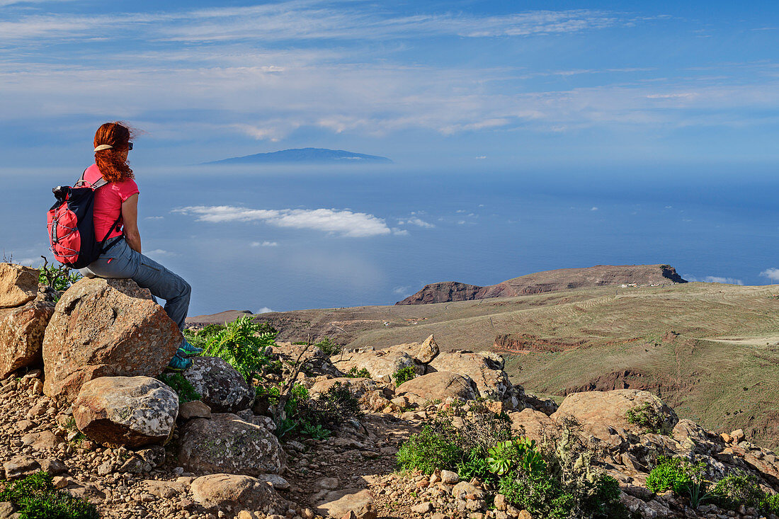 Frau beim Wandern sitzt auf Fels und blickt auf El Hierro, am Fortaleza, La Gomera, Kanarische Inseln, Kanaren, Spanien