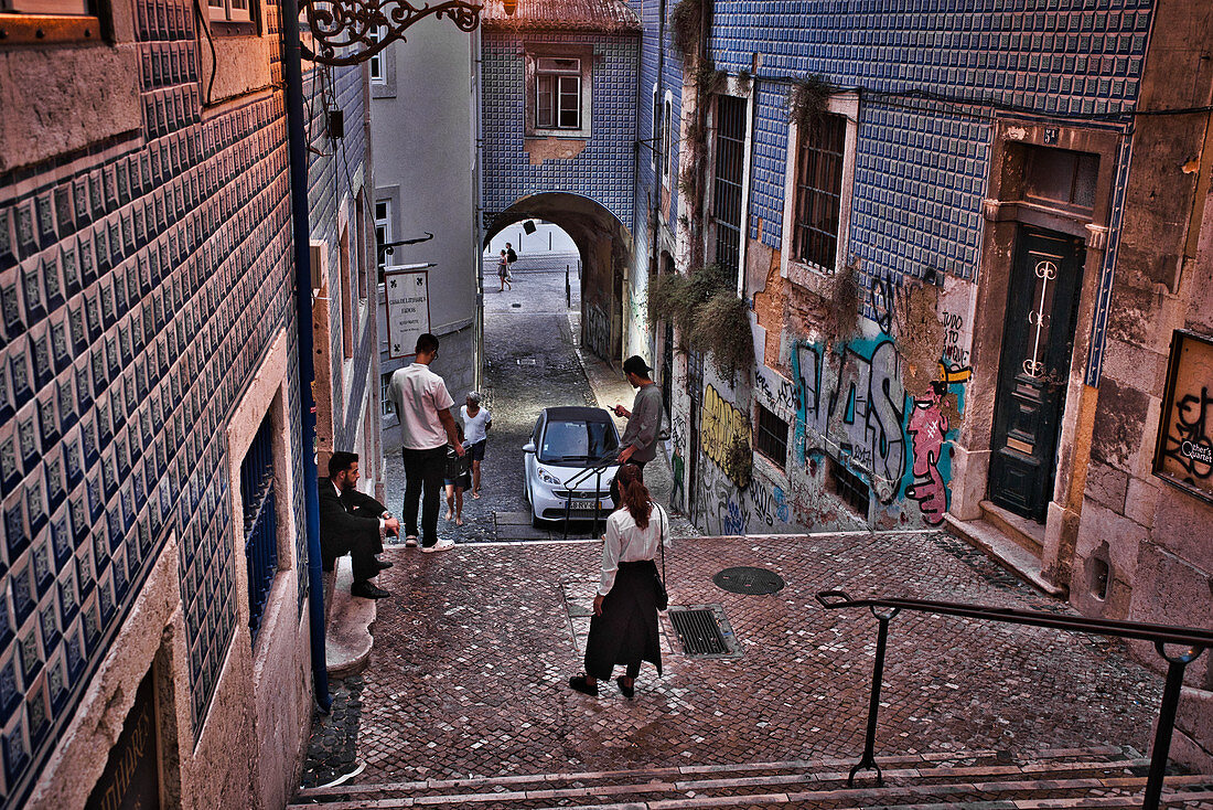 Menschen am Abend schauen auf ihre Handys auf einer Treppe in der Alfama, Lissabon, Portugal