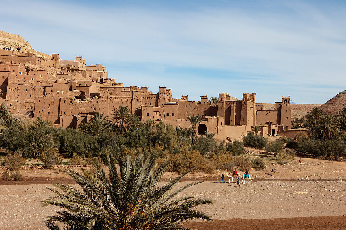 Touristen auf Kamelen vor den Mauern der Kasbah Ait Ben Haddou und die Wüste, Ait Ben Haddou, Marokko