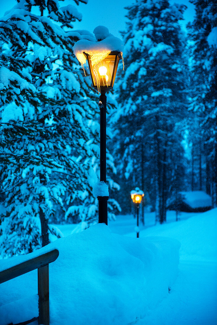 Mit Laternen beleuchteter verschneiter Weg zu einer Holzhütte bei Heggenes, Norwegen