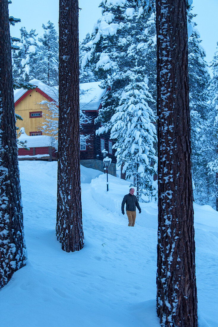 Mann läuft auf zugeschneiter Einfahrt Richtung Wald, Heggenes im Winter, Norwegen