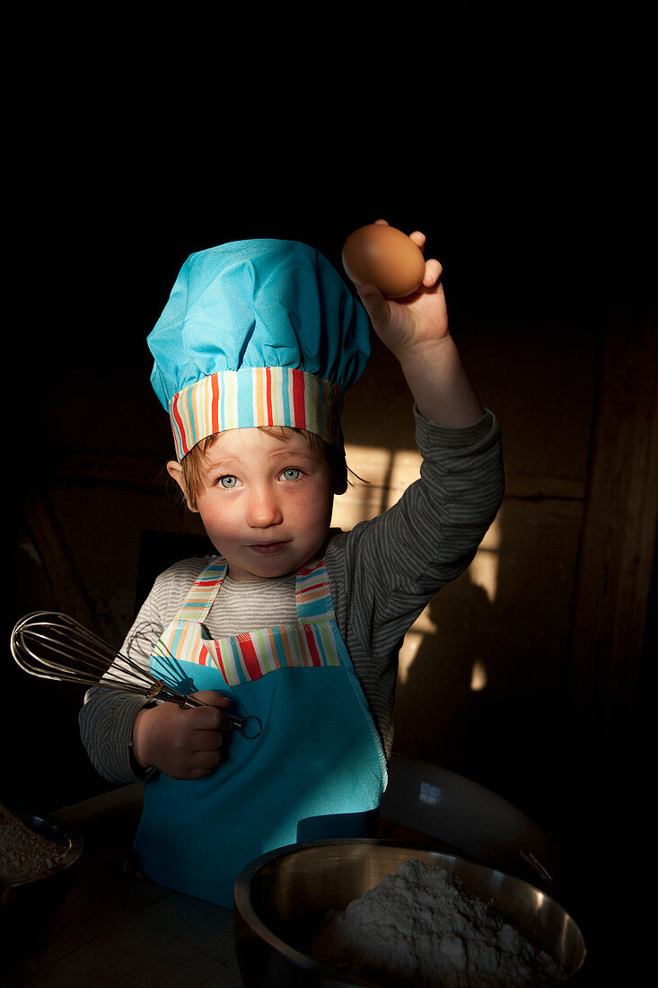 Portrait cute girl in chefs hat baking, holding egg