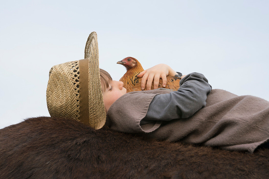 Girl hugging chicken, laying on horse