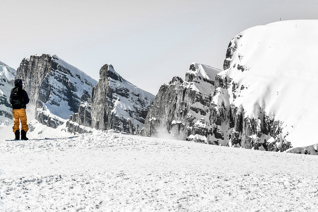 Mann mit Rucksack steht vor einer verschneiten Bergkulisse in der Schweiz, Churfirsten, Chäserrugg