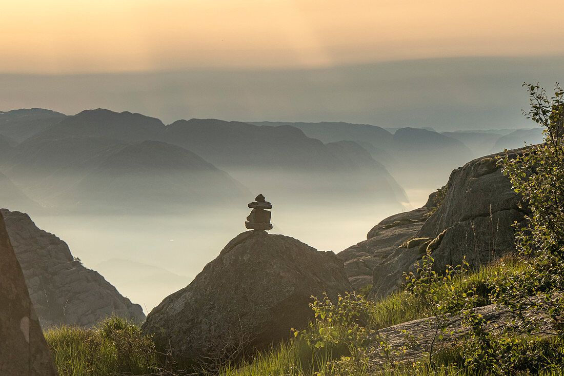 Cairn stands on a rock in the sunrise. In the background mountains in the morning fog and the Lysefjord. Norway