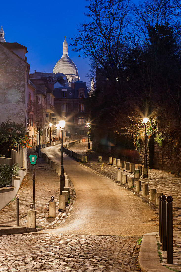 A small street in Montmatre at night with illuminated Sacre Coeur Basilica in the background. Paris, France