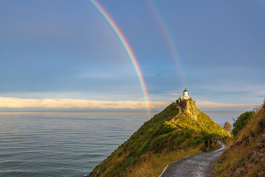 Doppelter Regenbogen über Nugget Point-Leuchtturm nach dem Sturm. Ahuriri-Ebene, Clutha-Bezirk, Otago-Region, Südinsel, Neuseeland