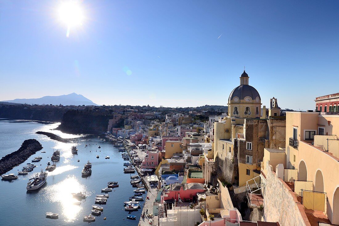 Backlit view of the small harbor of Corricella on the island of Procida. In the background the island Ischia, Campania, Italy