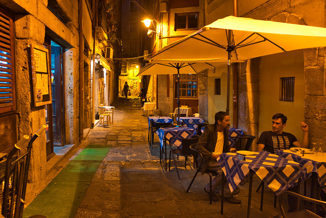 Tische eines kleinen Restaurants mit zwei Männern am späten Abend in den Gassen des Cais da Ribeira, Porto, Portugal